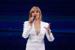 Milly Carlucci vestita di bianco che parla al microfono