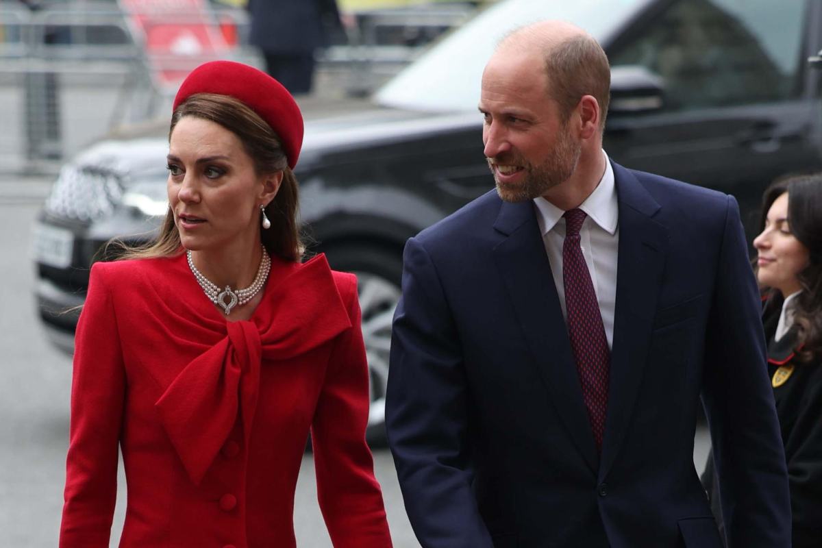 Kate con espressione interdetta e cappotto rosso, William con un completo e sorridente